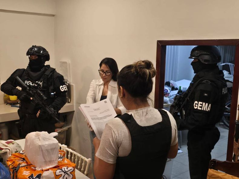 Luisa González durante el operativo de detención en su vivienda en Canuto, mientras una funcionaria sostiene un documento frente a ella y dos agentes del GEMA custodian el lugar.
